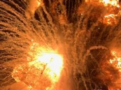 Cenas caóticas enquanto uma fábrica entra em chamas, lançando blocos de concreto e um tanque de produtos químicos no ar